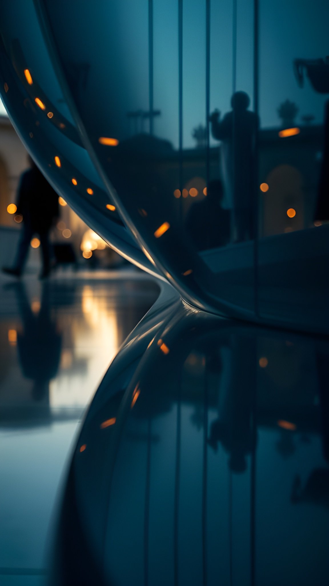 A creative photograph of a blue glass curve in a lobby with warm lights and people silhouettes