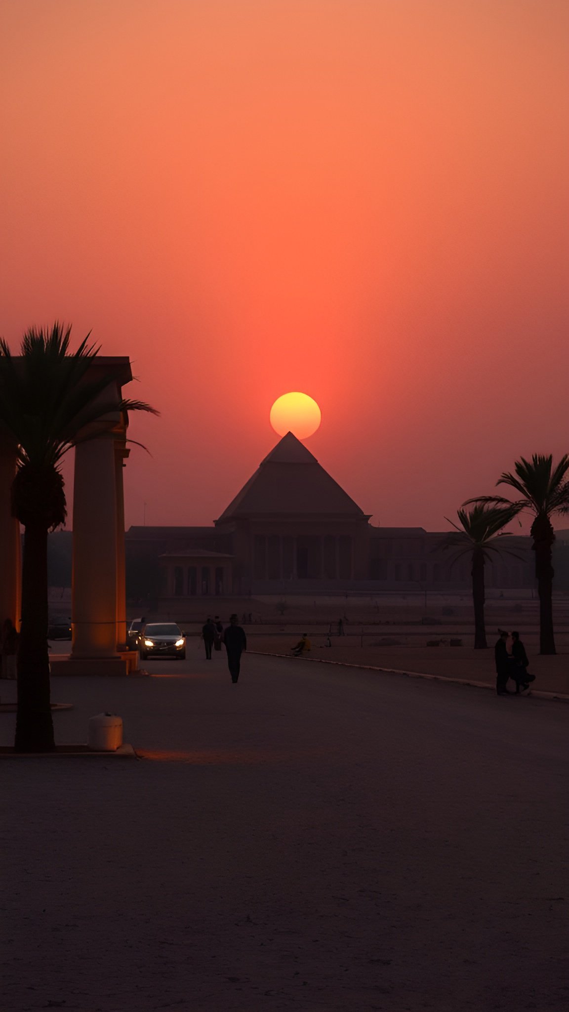 Pyramid silhouetted against sunset with palm trees and museum building in foreground