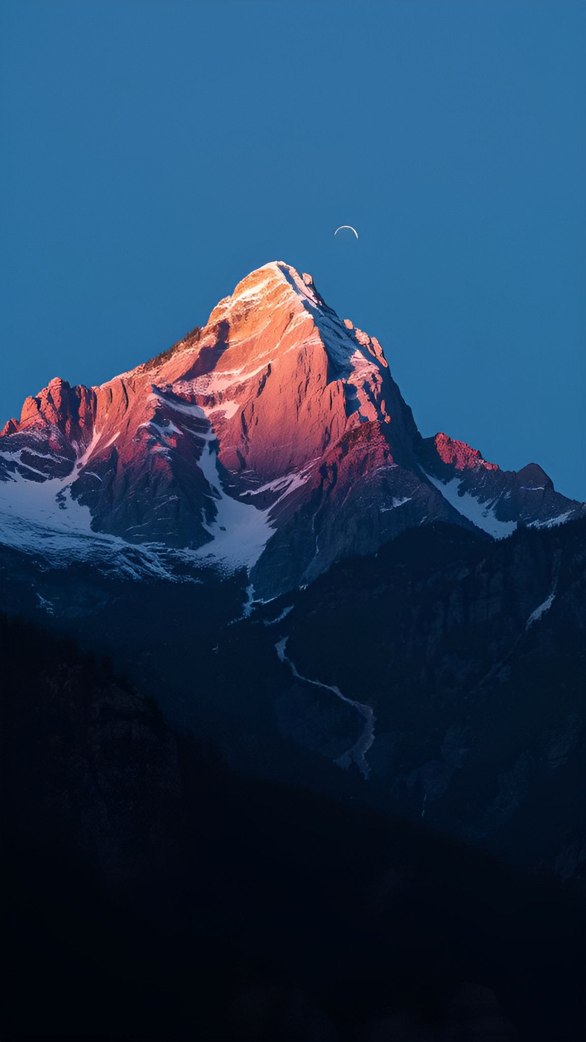 Snow-capped mountain peak glowing in alpenglow with crescent moon above